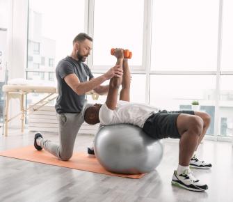 Athlete working out with physical therapist on exercise ball with small weights