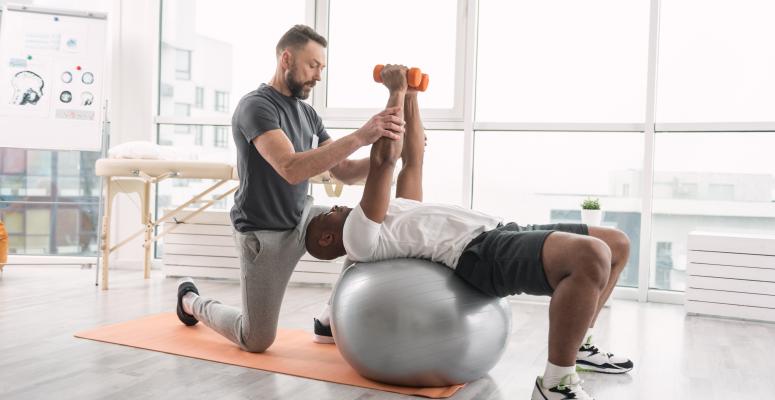 Athlete working out with physical therapist on exercise ball with small weights